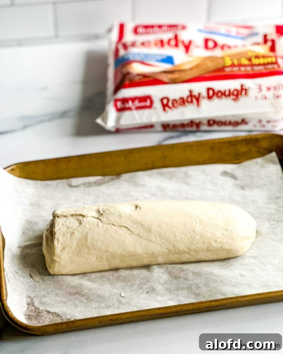 A loaf of frozen pizza dough resting on a parchment-covered sheet pan, slowly thawing.