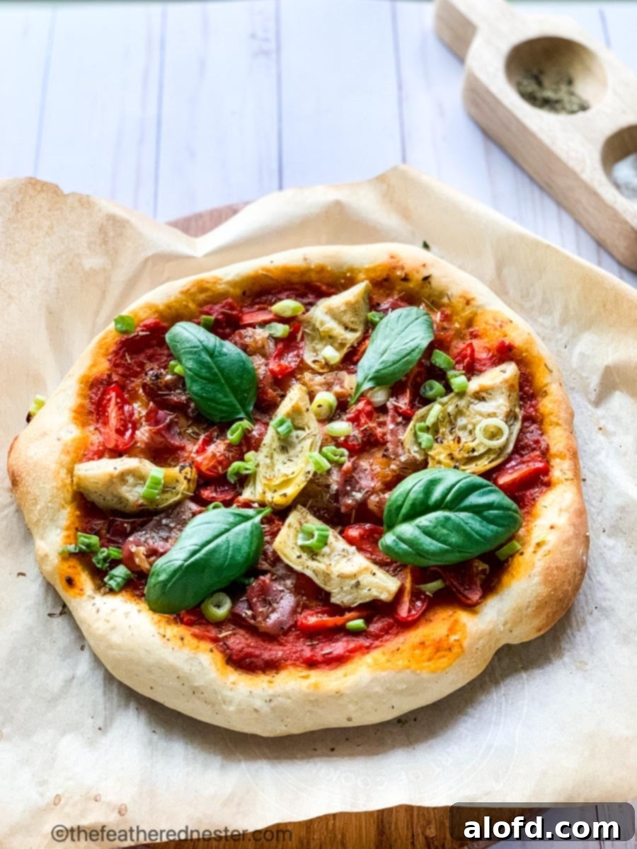 A delicious baked vegan pizza topped with vibrant marinara sauce, tender artichokes, colorful bell pepper, and sweet cherry tomatoes, garnished with fresh basil.