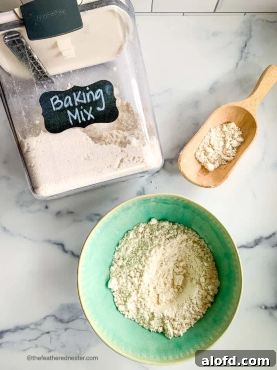 Simple Homemade Bisquick Mix 7 A green bowl filled with DIY baking mix, alongside a clear Prepworks container holding mixed homemade Bisquick baking mix and a wooden scoop of the scratch mix, highlighting storage.