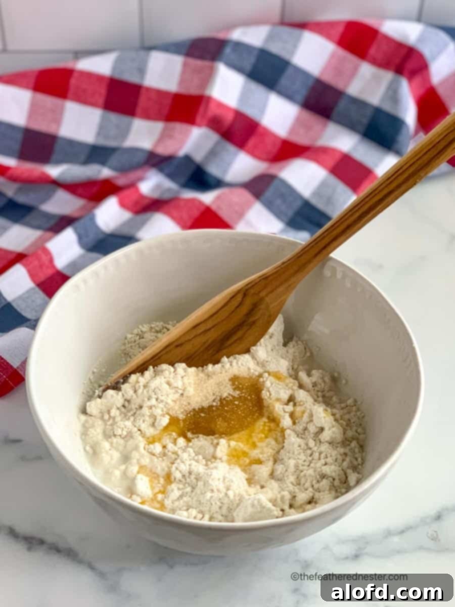 A wooden spoon rests in a bowl of creamy biscuit batter, ready to be dropped onto the cherry filling for a Bisquick dessert. The smooth texture of the batter promises a tender and delicious topping.