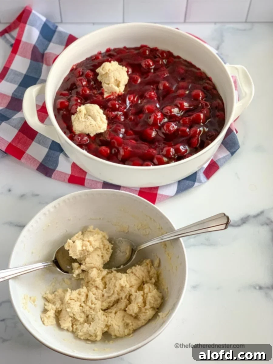 A bowl of light, fluffy biscuit batter sits in front of a casserole dish filled with vibrant red cherry pie filling, awaiting its topping for the Bisquick dessert.