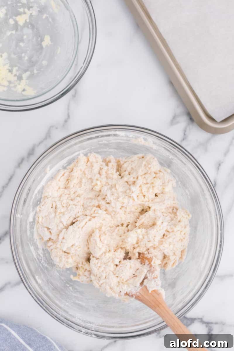 Homestyle Buttermilk Biscuits 6 Using a wooden spoon to mix sticky dough in a glass mixing bowl, showcasing the ideal texture for biscuits.