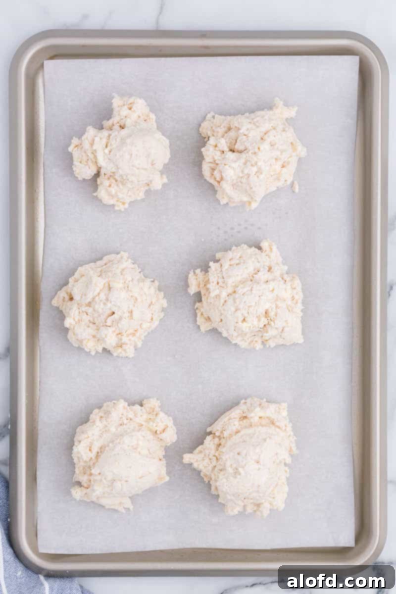 Homestyle Buttermilk Biscuits 7 Unbaked drop biscuits neatly arranged on a parchment-lined baking sheet, ready for the oven.