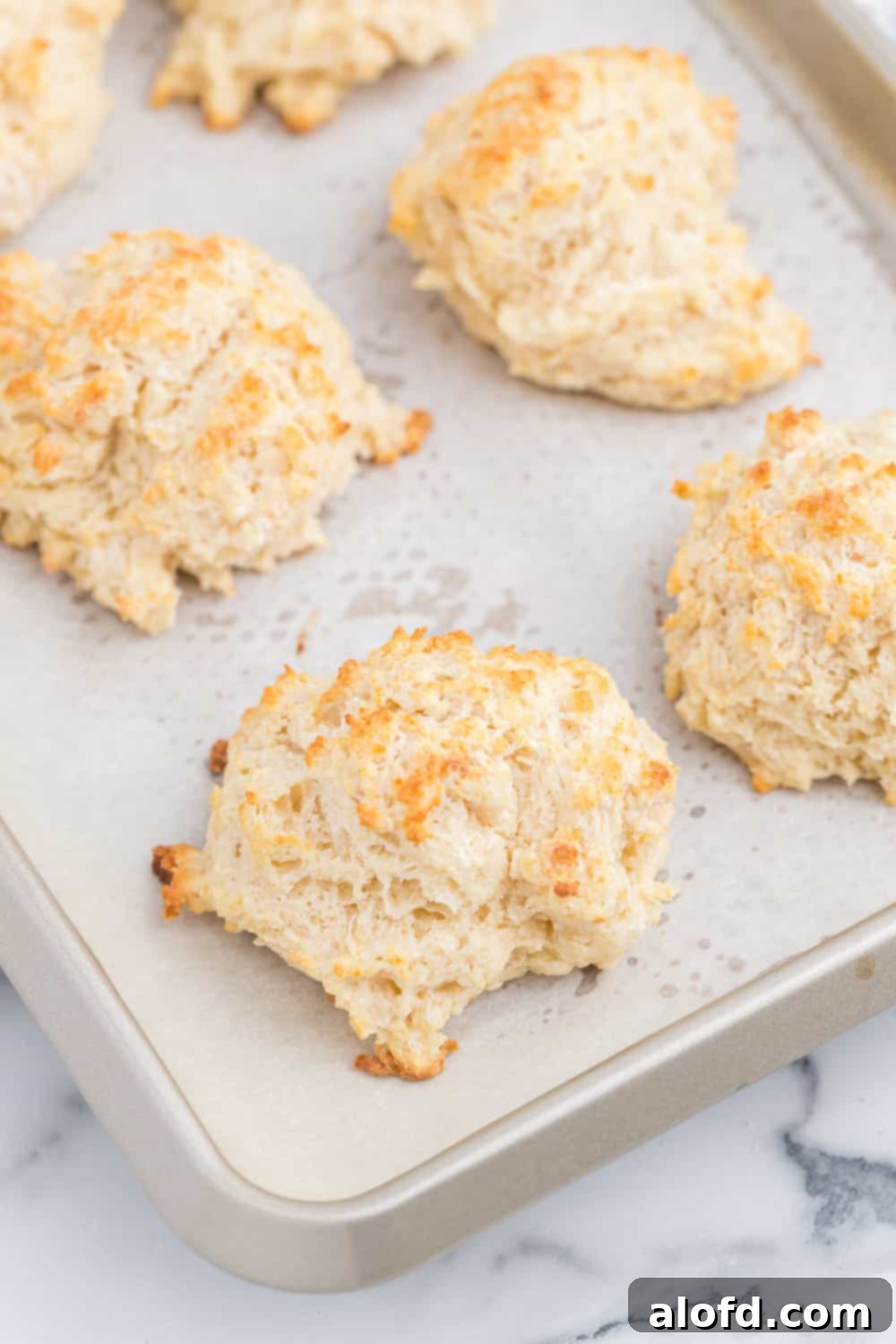 Homestyle Buttermilk Biscuits 8 A fresh batch of homemade drop biscuits cooling on a baking sheet, showcasing their golden crust and fluffy texture.