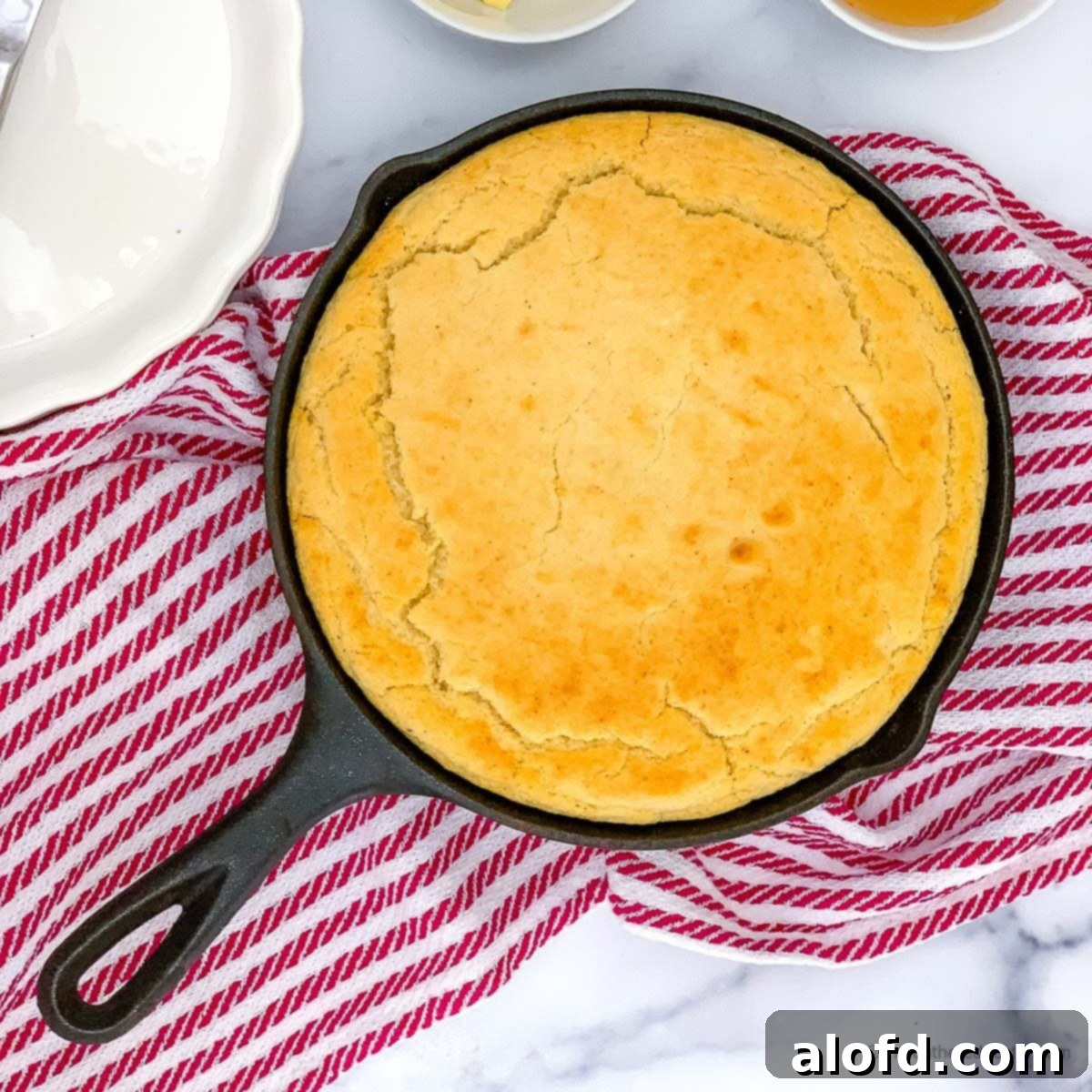 a cast iron skillet with cornbread with self rising flour and a striped red kitchen towel at the back.