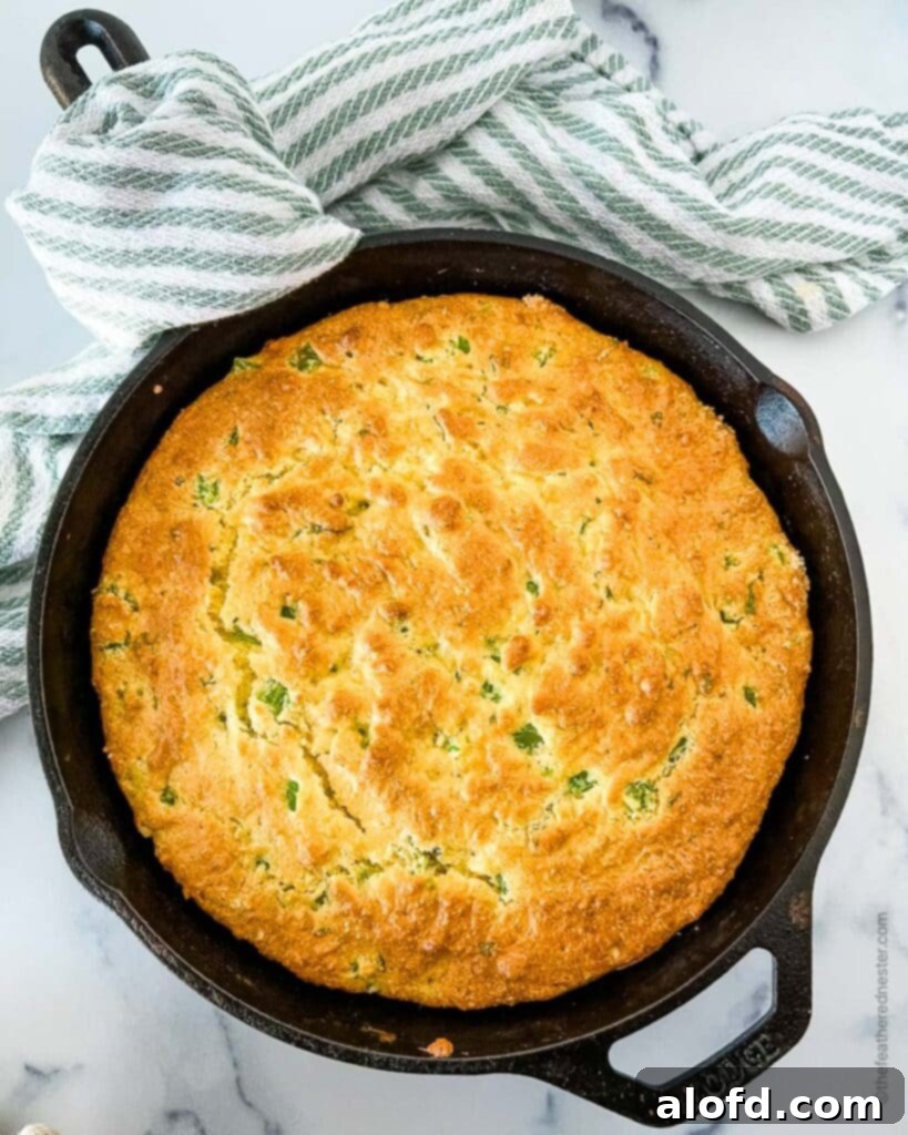 baked Jiffy jalapeno cheddar cornbread in a skillet with a striped cloth in the background.