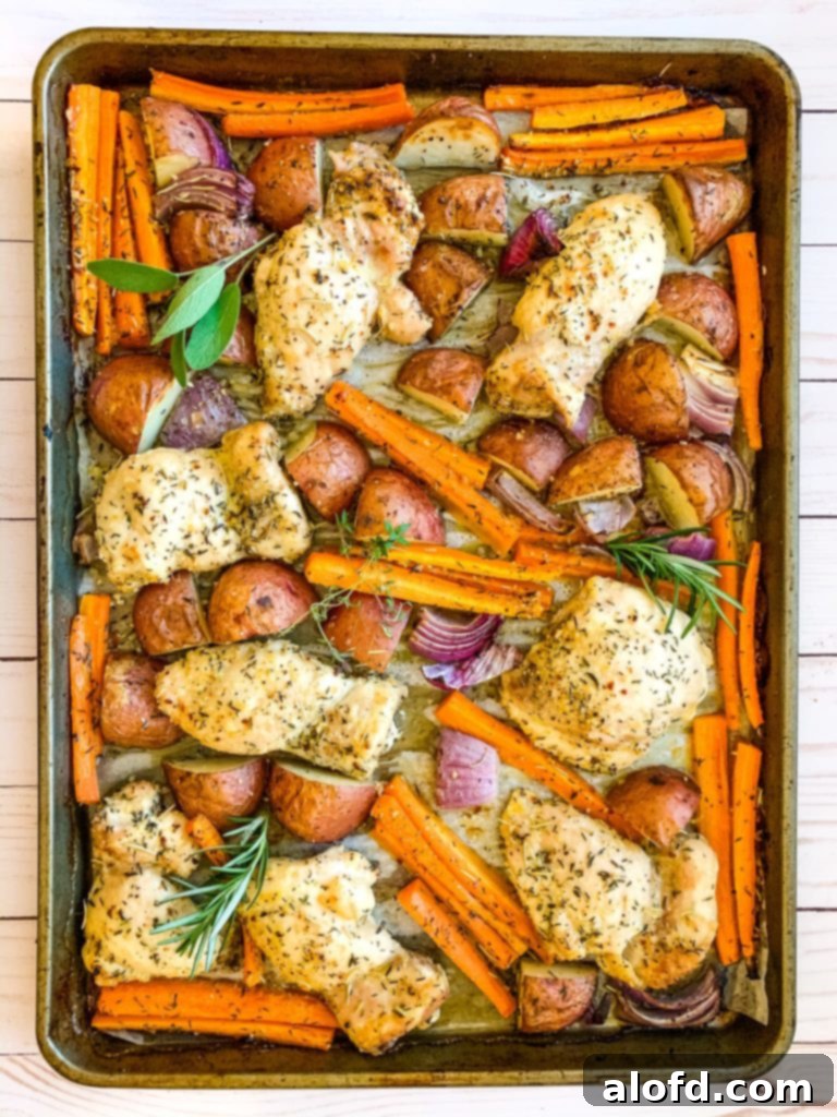 Crispy chicken thighs and colorful roasted vegetables on a baking sheet, ready to serve.