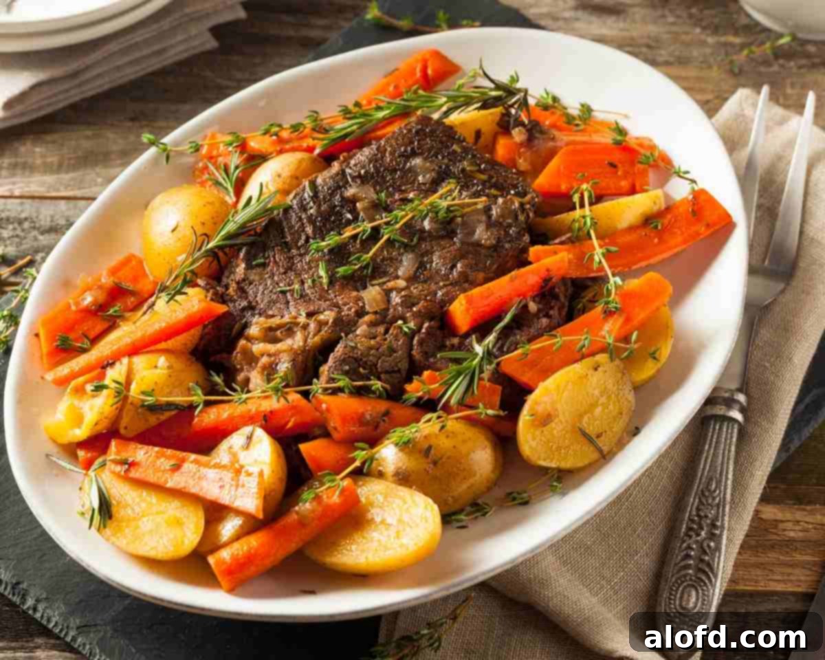 Meltingly Tender Slow Cooker Chuck Roast 7 A generous serving of crockpot chuck roast with mixed vegetables on a white plate, with a full platter of roast in the background, ready for a family meal.