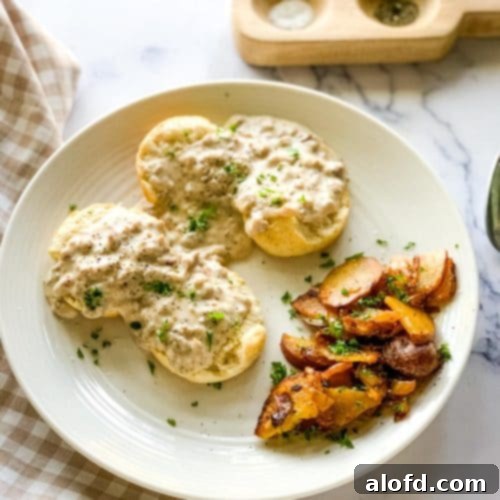 Fluffy Biscuits with Creamy Sausage Gravy 2 a plate of sausage gravy and biscuits with potatoes and a checked napkin and salt and pepper.