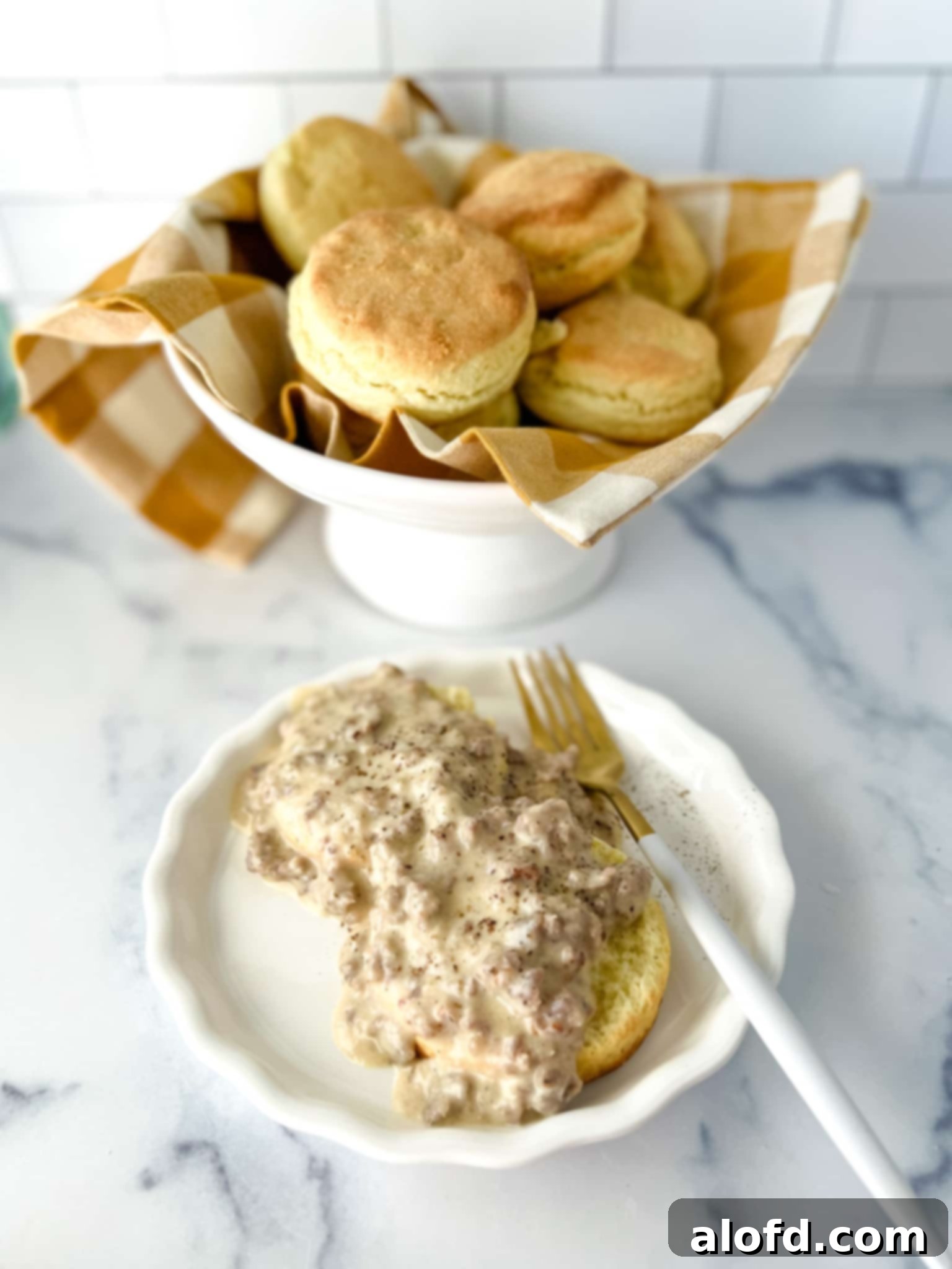Fluffy Biscuits with Creamy Sausage Gravy 5 A plate of biscuits topped with gravy and a bowl of biscuits.