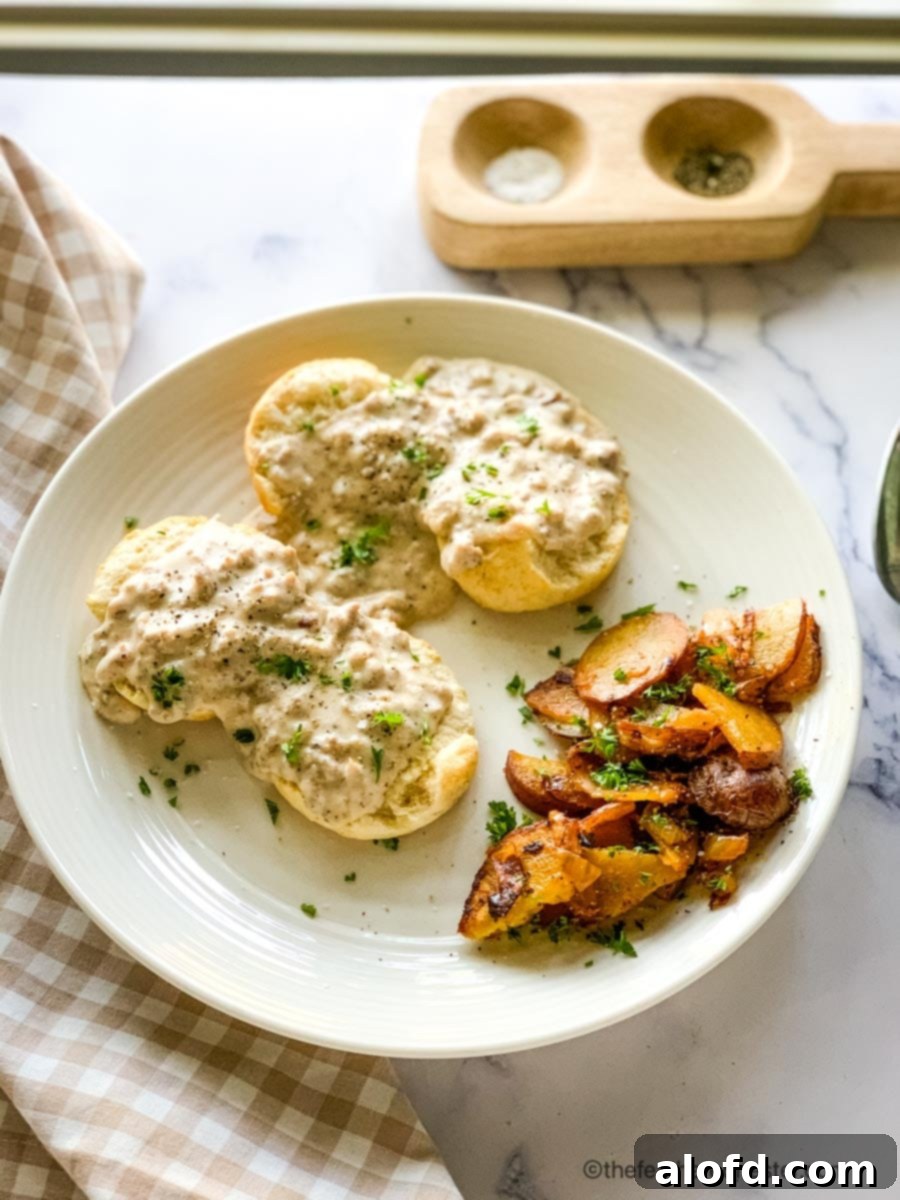 Fluffy Biscuits with Creamy Sausage Gravy 8 a plate of sausage gravy and biscuits with potatoes and a checked napkin and salt and pepper.