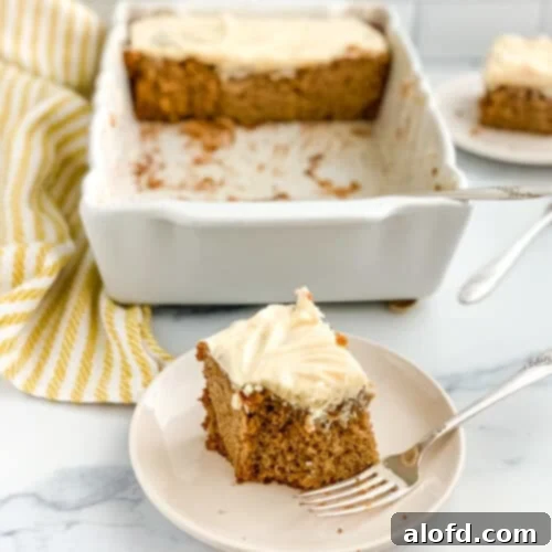 A plated slice of sourdough apple cake with the full pan behind it, showcasing the cake's delicious texture and frosting.