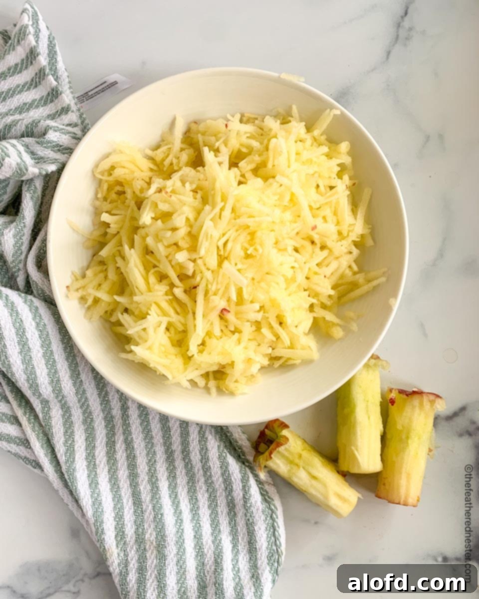 A vibrant green bowl brimming with freshly grated apples, resting on a stylish gray and white striped kitchen towel.