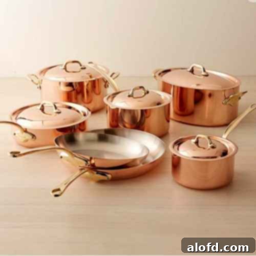 A luxurious collection of Mauviel Copper M’150 B cookware, featuring various sized pots and pans with gleaming copper exteriors and elegant brass handles, representing the finest in French culinary tradition.