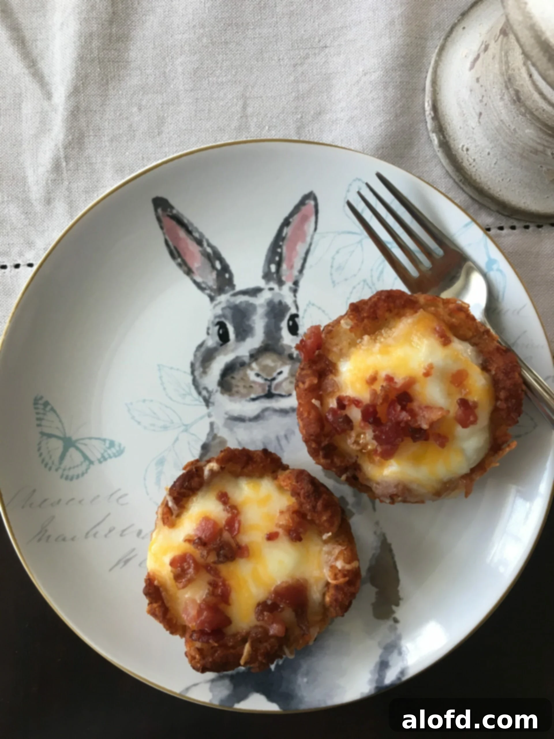 Crispy Tater Tot Egg Bites 2 Golden-brown tater tot egg nests, filled with perfectly cooked eggs, and sprinkled with fresh herbs, resting on a charming bunny-themed plate. Ideal for Easter or any festive brunch.