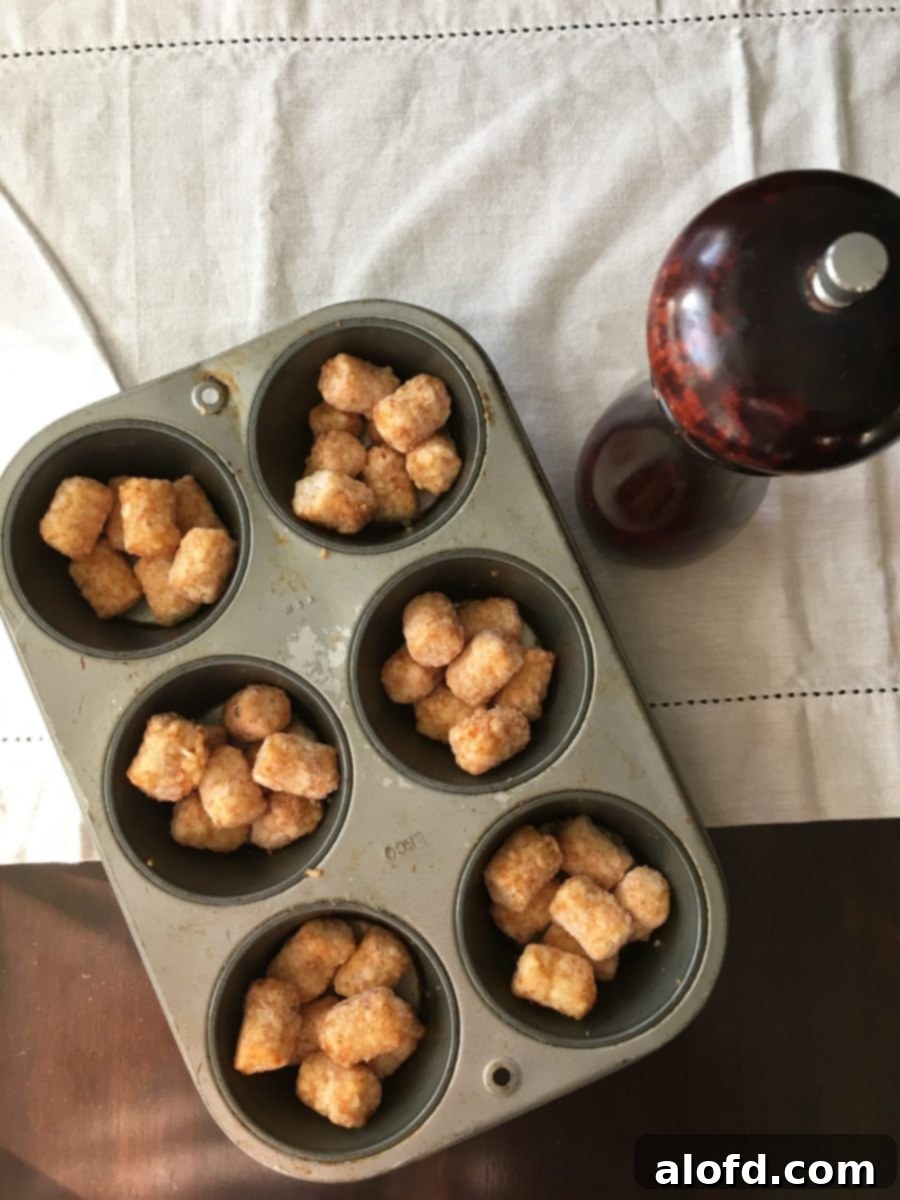 Crispy Tater Tot Egg Bites 3 A jumbo muffin pan with precisely arranged frozen tater tots in each well, perfectly spaced and ready for their initial bake to create crispy bases.