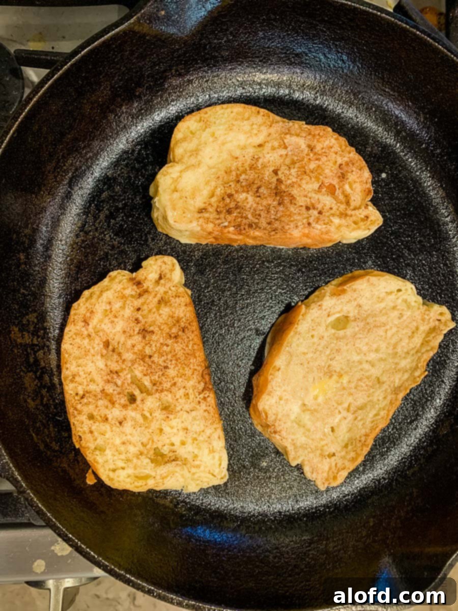 Tangy Sourdough French Toast 6 Three pieces of French toast cooking in a cast iron skillet.