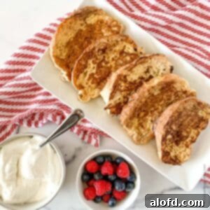 Tangy Sourdough French Toast 9 a white platter with slices of French toast, a small bowl of berries and whipped cream set on a red and white striped napkin.