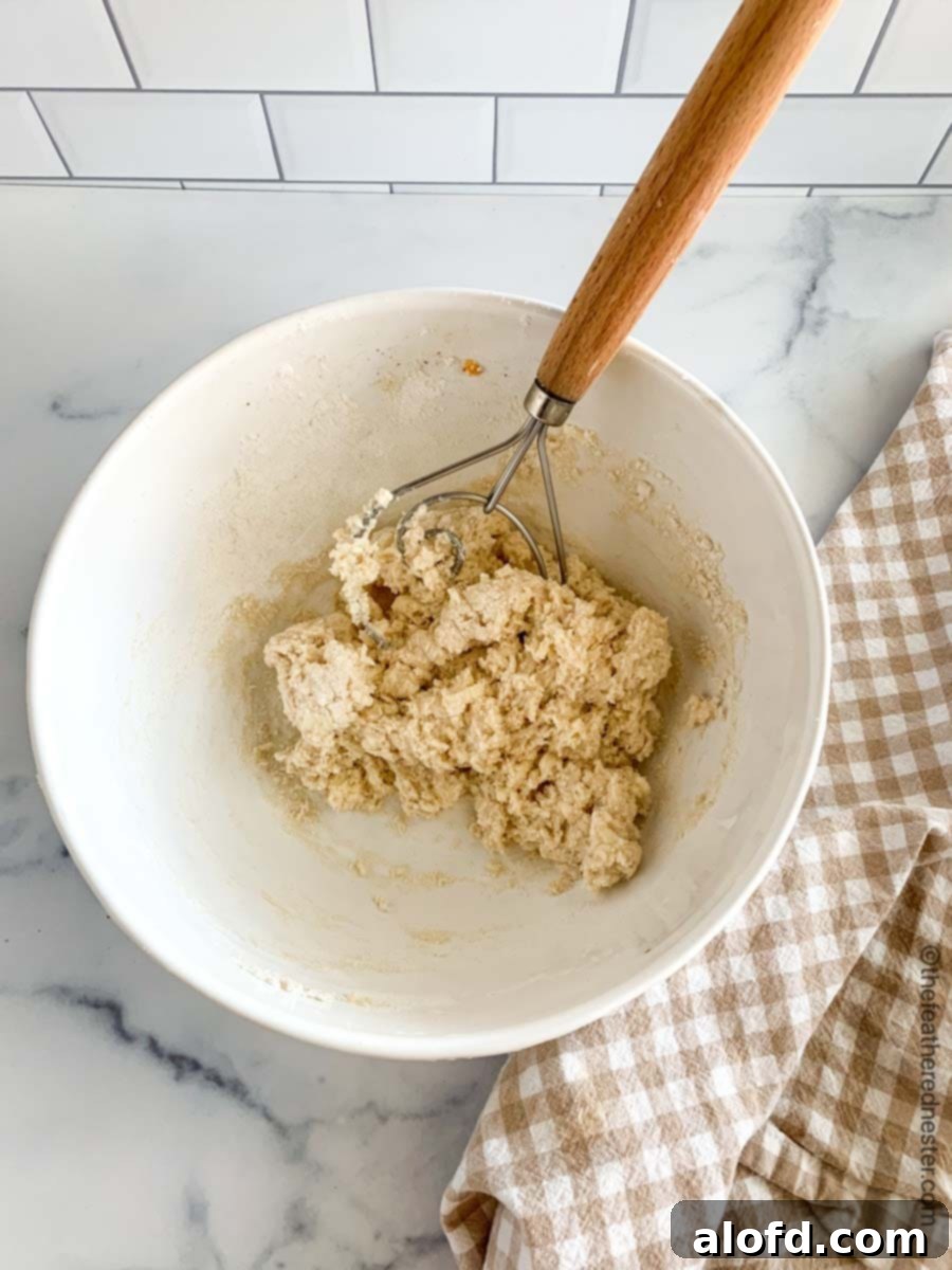 Easy Bisquick Peach Cobbler 5 A white bowl with a whisk and the mixed ingredients for the fluffy biscuit topping of the peach cobbler, showing its thick consistency.