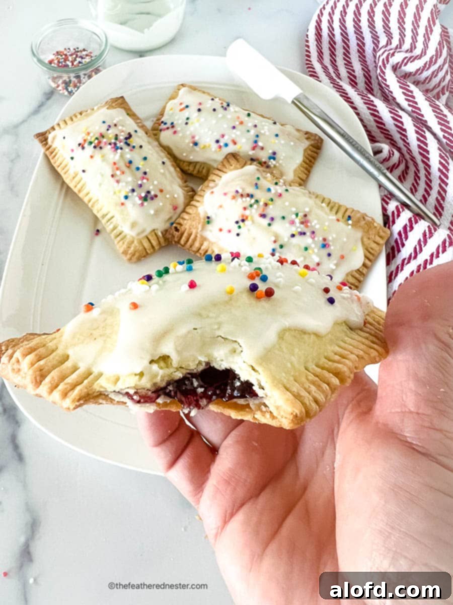 Untamed Berry Breakfast Pastries 9 A close-up of a homemade blueberry pop tart held in a hand, showcasing its flaky crust and frosted top.