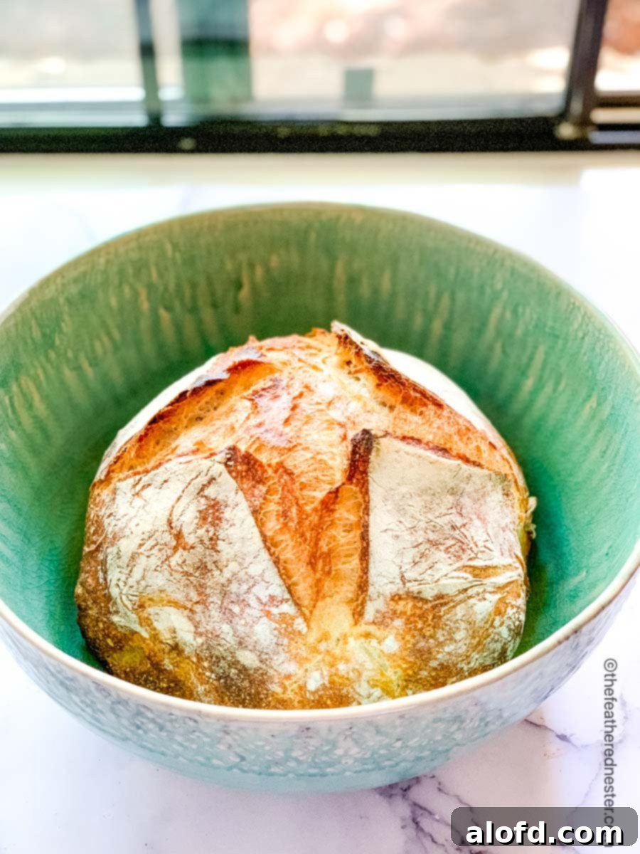 A loaf of overnight sourdough bread in a green bowl, ready for slicing.