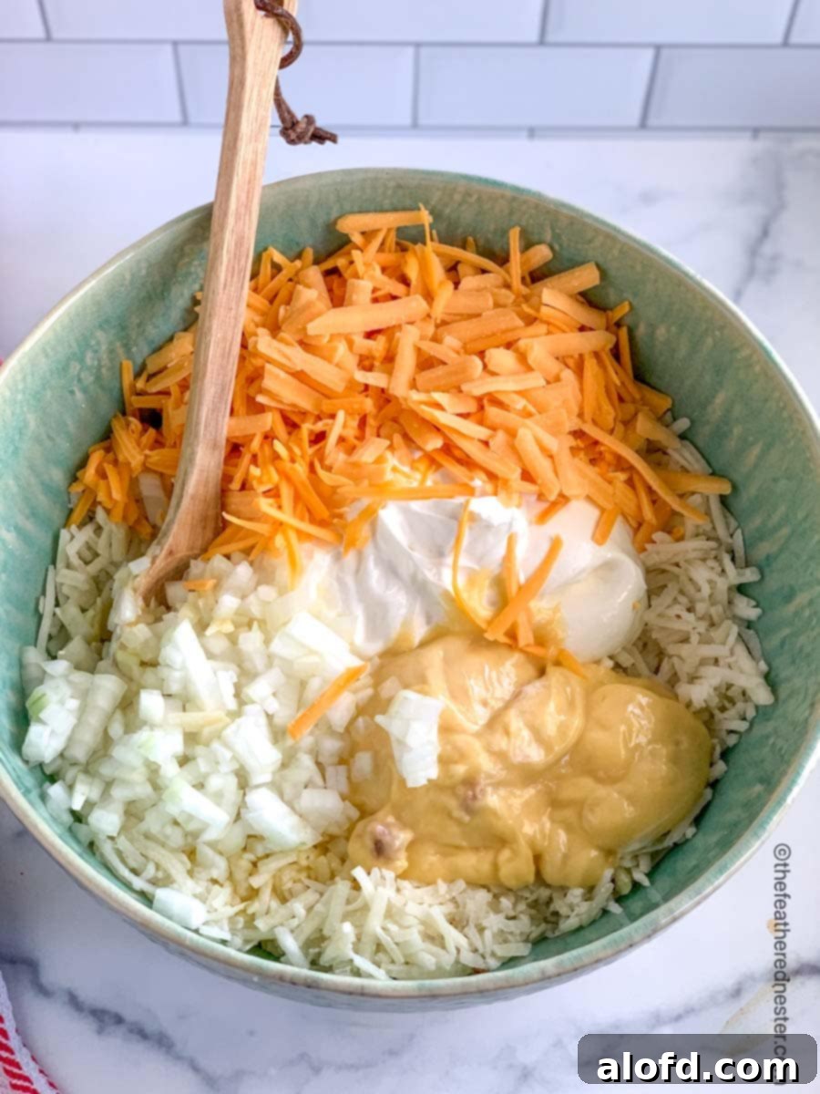 Homestyle Hash Brown Casserole 3 A bowl filled with the key ingredients for hash brown casserole: shredded potatoes, sour cream, grated cheese, cream of chicken soup, and melted butter.