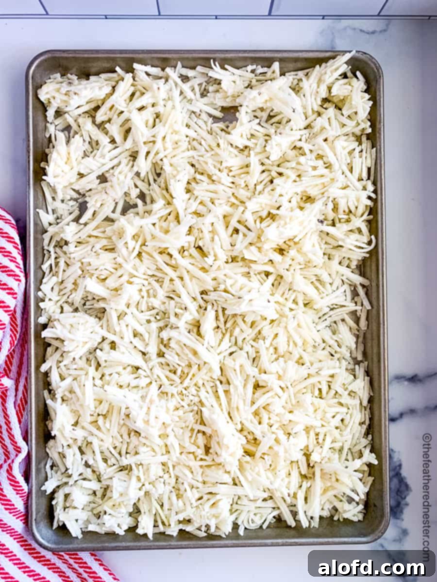 Homestyle Hash Brown Casserole 5 A baking sheet filled with a layer of thawed shredded hash brown potatoes, ready for mixing into the casserole.