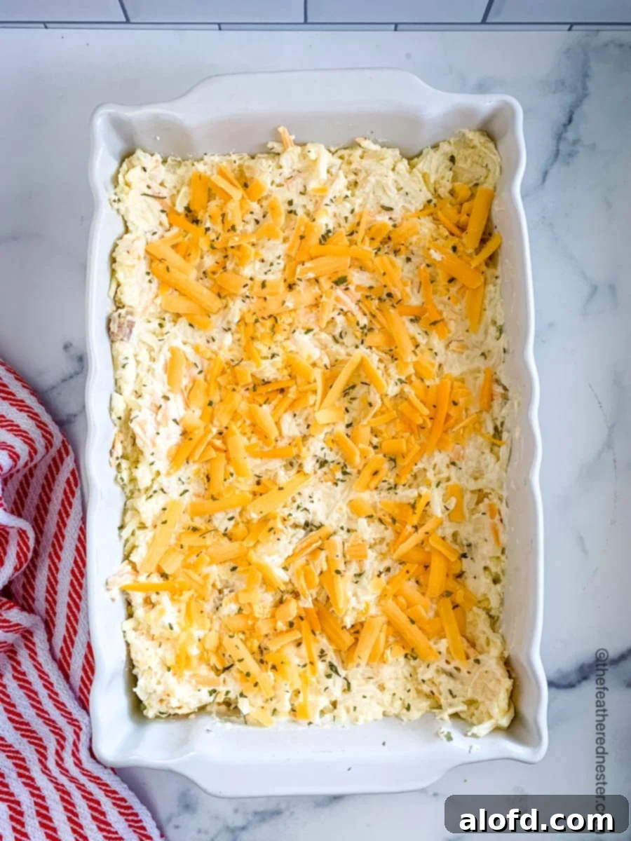 Homestyle Hash Brown Casserole 6 Hash brown casserole mixture being poured into a white baking dish before baking, with shredded cheese on top.
