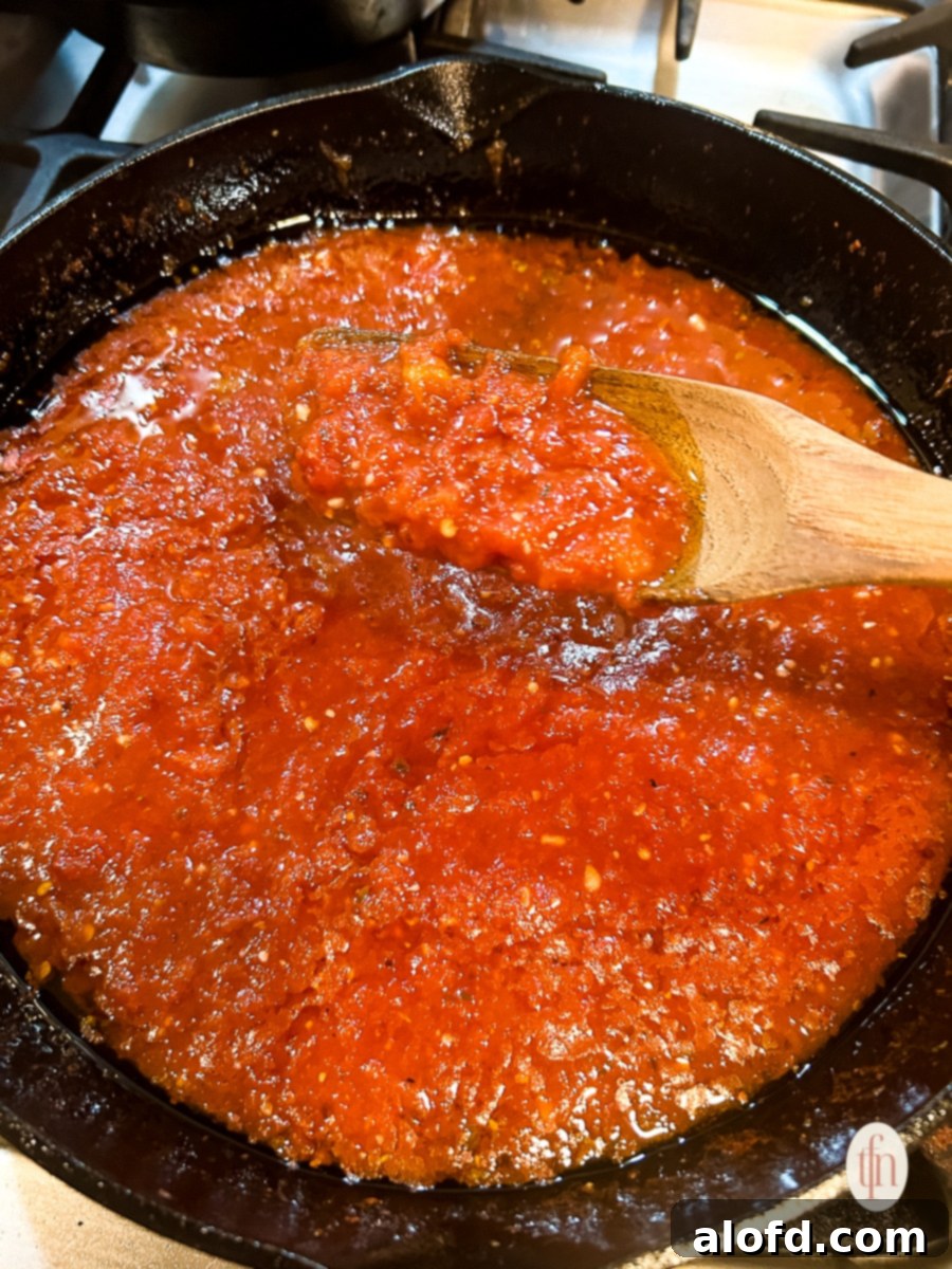Wooden spoon holding up tomato sauce over a pan of simmering sauce.