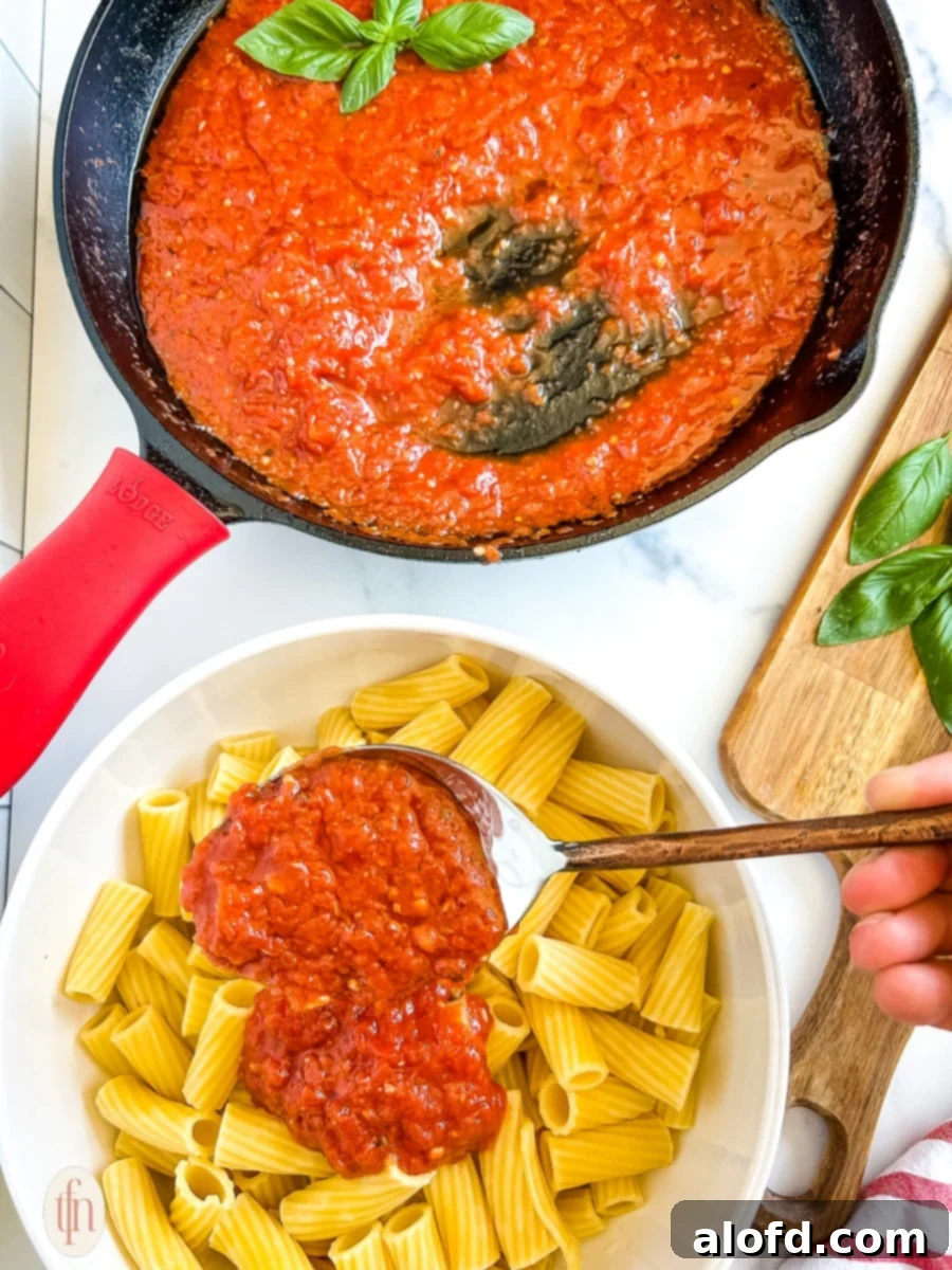 Spooning tomato sauce over a bowl of pasta on a white background.