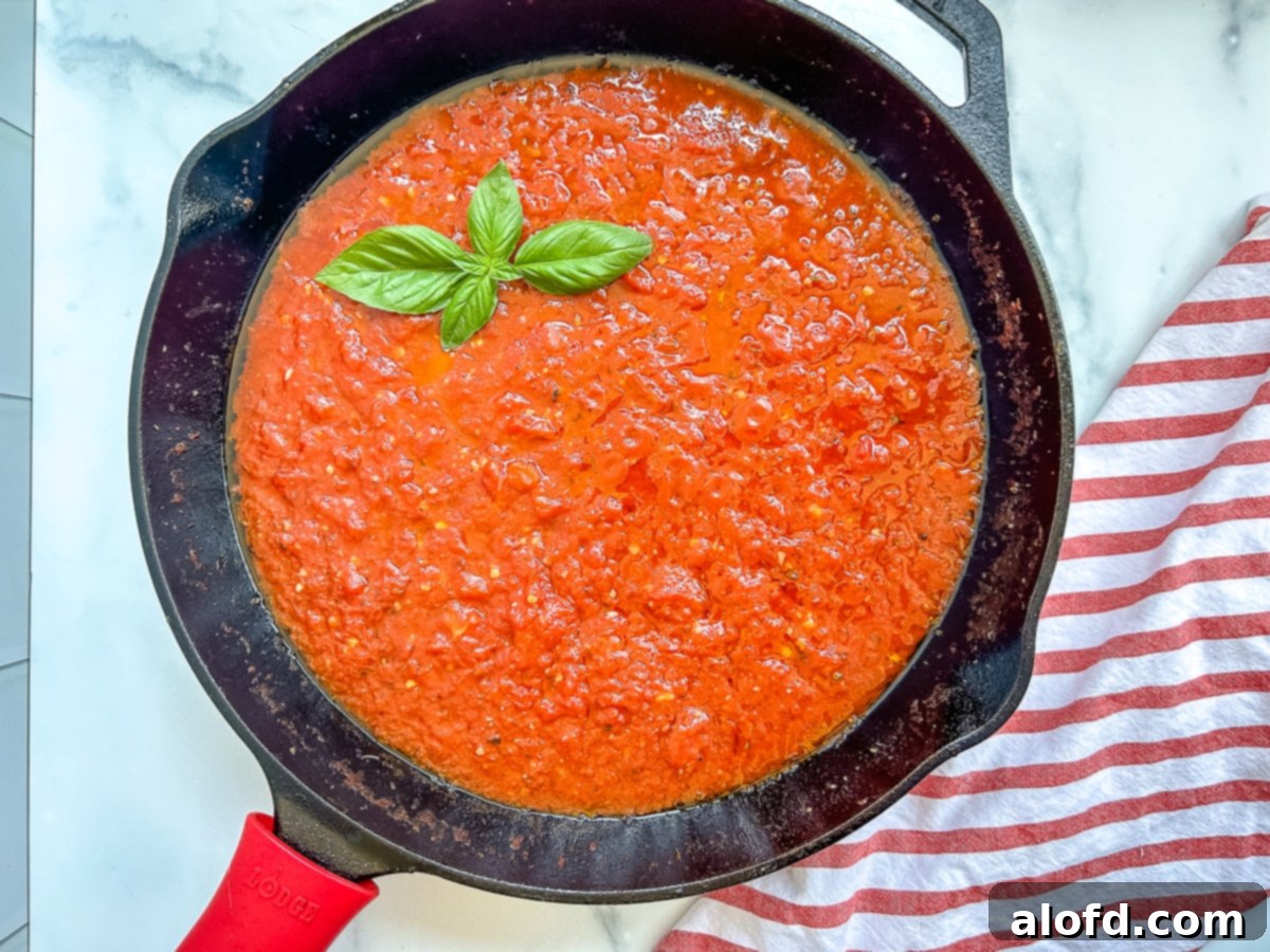 Italian sauce in a cast iron pan on with a sprig of basil on top.