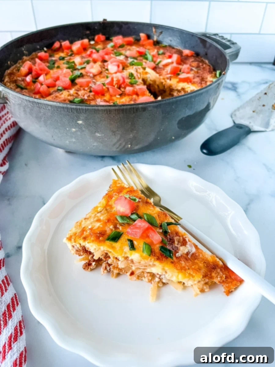 A perfectly baked slice of eggs with chorizo on a white plate with a fork, with a round cast iron pot containing more casserole in the background.