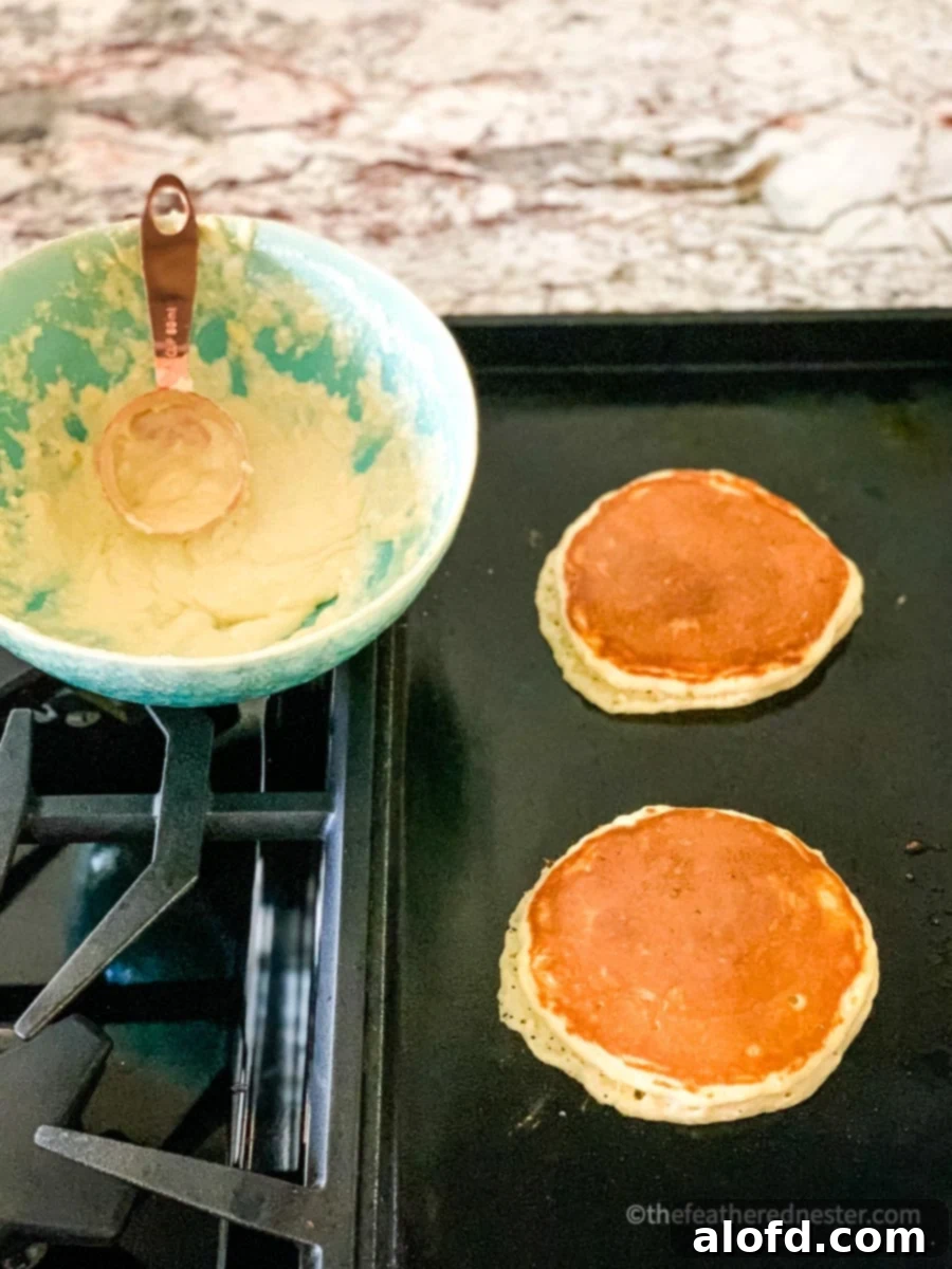 Pancakes gently cooking on a griddle, with a bowl of prepared batter visible in the soft background.