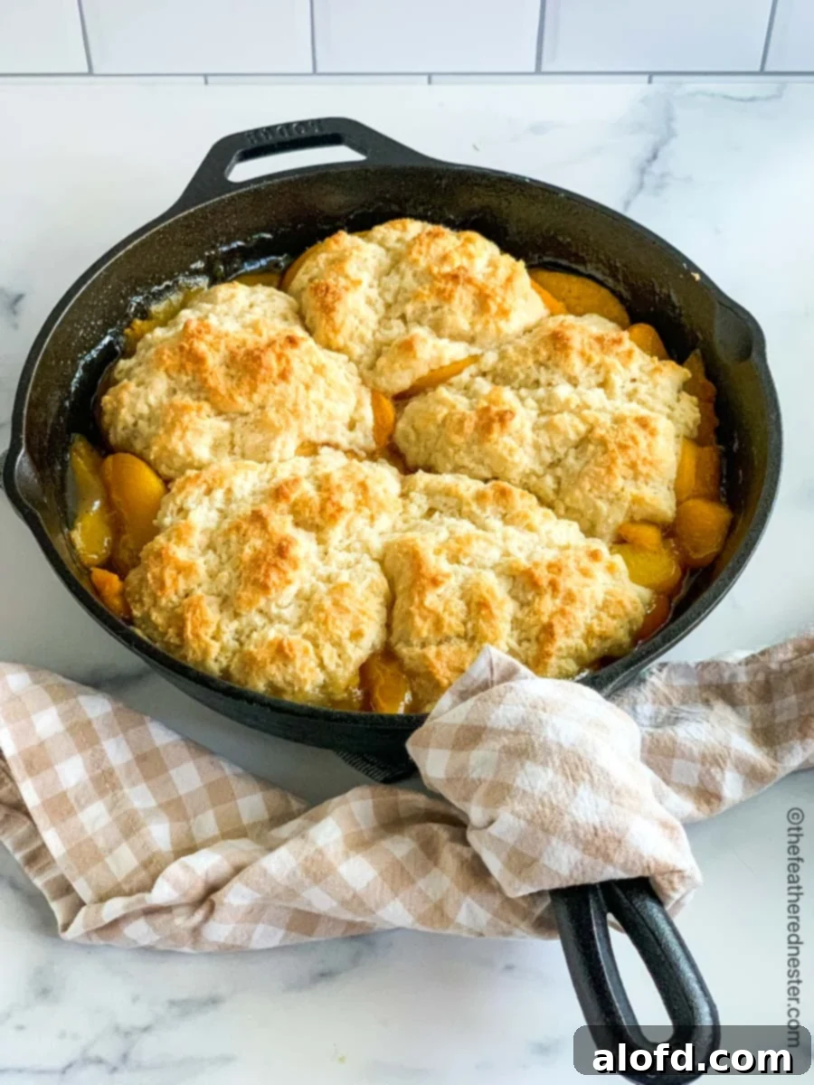 A cast iron skillet of bubbling, golden peach cobbler, glistening with fruit and a perfect biscuit topping.