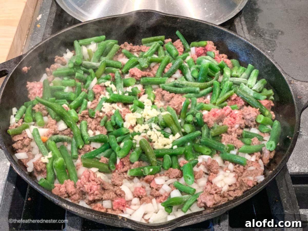 Crispy Tater Tot Green Bean Bake 5 A skillet of ground beef, green beans, and onions sautéing in a pan.