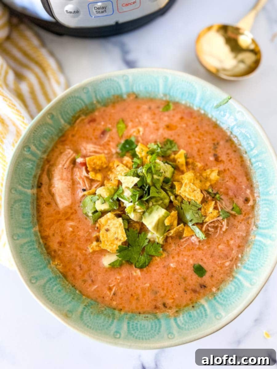 A green bowl brimming with Instant Pot Tortilla Soup, set next to a vibrant striped yellow cloth, the Instant Pot itself, and a gleaming golden spoon, creating an inviting and cozy scene.