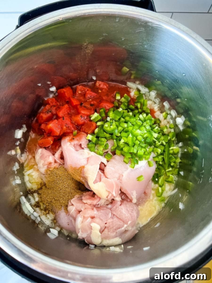 A curated display of ingredients for making creamy chicken tortilla soup, featuring chicken stock, tender chicken breast, vibrant jalapeno peppers, a crisp onion, fragrant garlic, fire-roasted diced tomatoes, rich cream cheese, aromatic cumin, and golden olive oil, all artfully arranged.