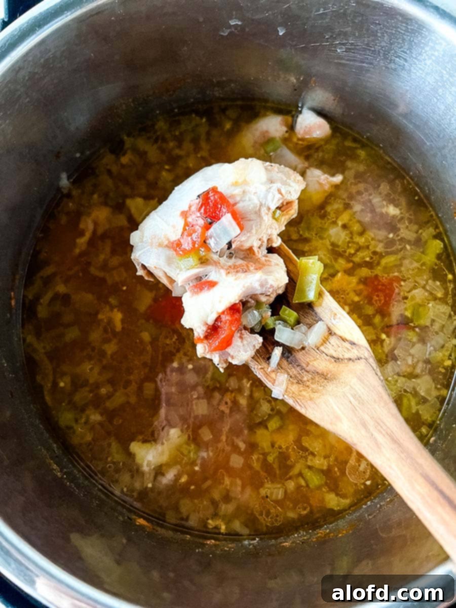 A wooden spoon gently scoops a piece of tender chicken from the Instant Pot, highlighting the perfectly cooked meat ready for shredding.