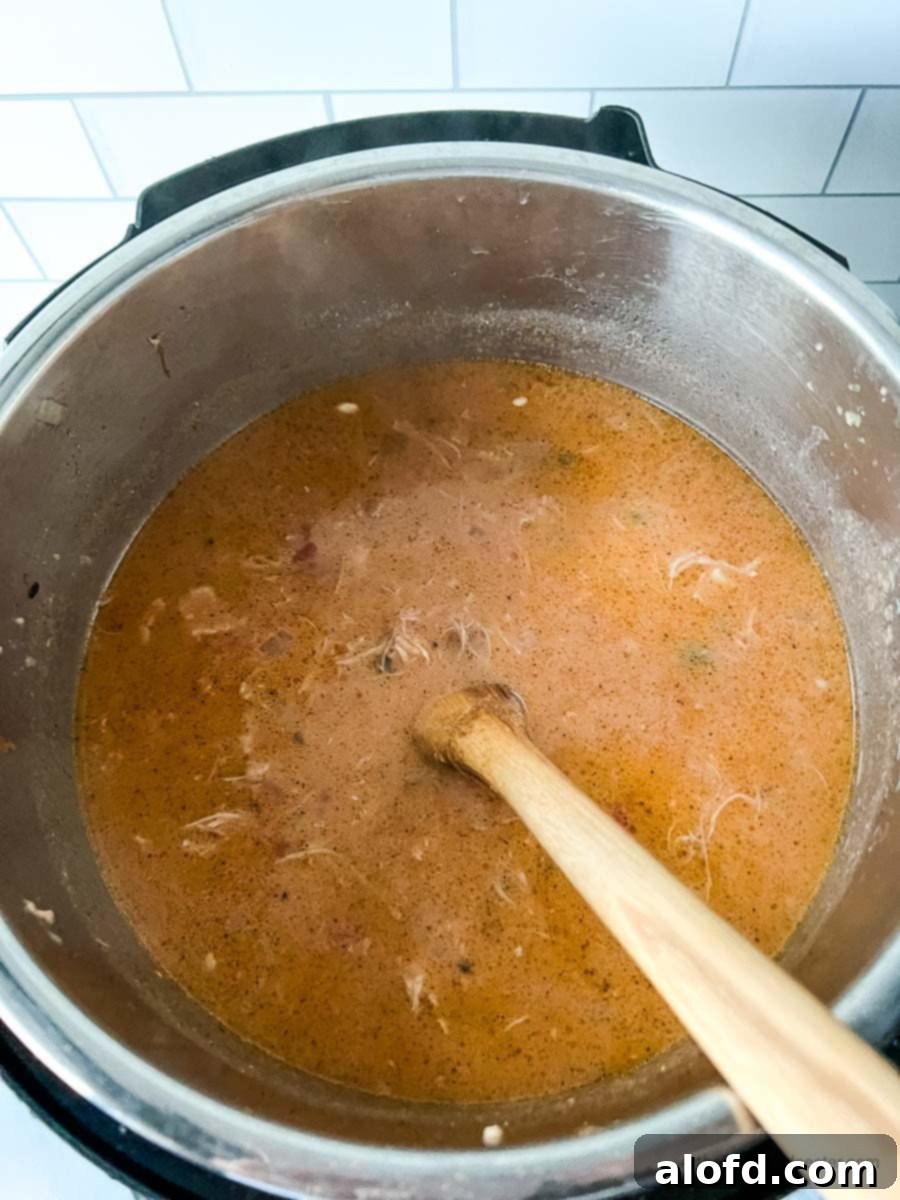 A block of cream cheese gently introduced into the Instant Pot, being stirred into the soup with a wooden spoon, creating a luscious and creamy texture.