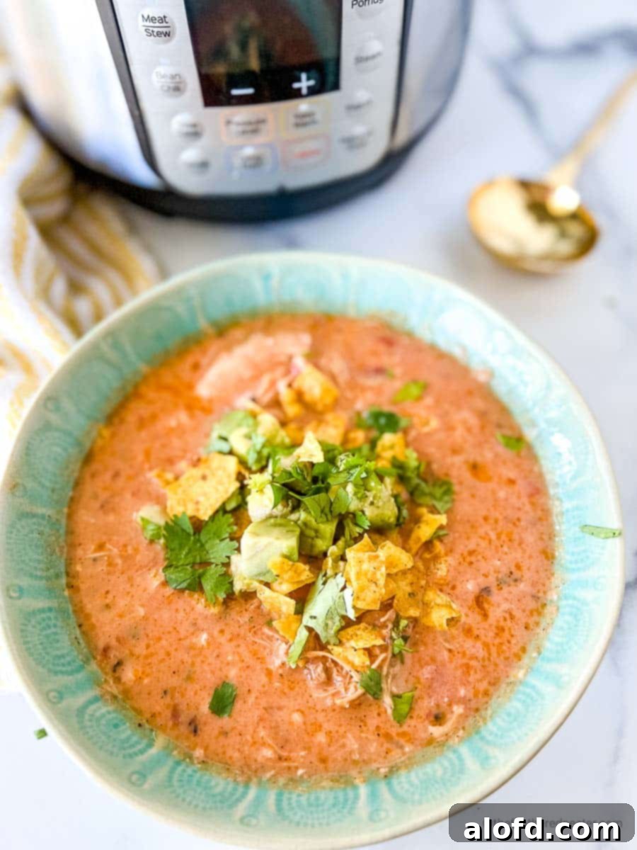 A close-up shot of a vibrant green bowl of Instant Pot tortilla soup, beautifully garnished, positioned beside an Instant Pot, a white and yellow striped napkin, and a gleaming gold spoon, evoking comfort and deliciousness.