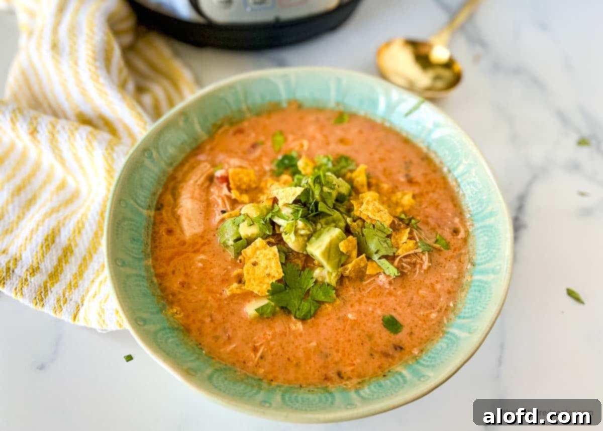 A horizontal view of a vibrant green bowl filled with Instant Pot Chicken Tortilla Soup, presented next to a striped yellow cloth, the Instant Pot itself, and a gleaming golden spoon, creating an appealing and warm tableau.