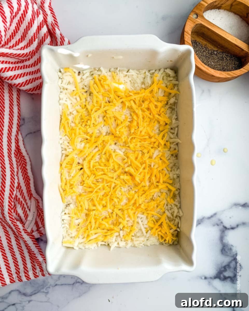 Ultimate Hash Brown Breakfast Bake 5 A casserole dish with an initial layer of hash browns and shredded cheese, ready for the oven.