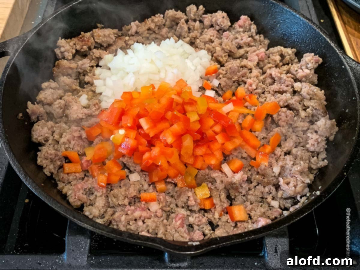 Ultimate Hash Brown Breakfast Bake 6 Sausage, bell pepper, and onion sizzling and sautéing in a skillet on the stovetop.