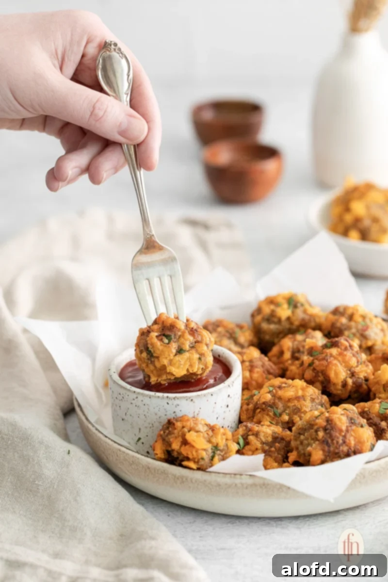 Bisquick Sausage Balls: Effortless Appetizer Perfection 9 A fork dipping a sausage ball into a small bowl of dipping sauce.
