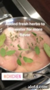 Chicken breasts poaching in a pan with water and herbs.