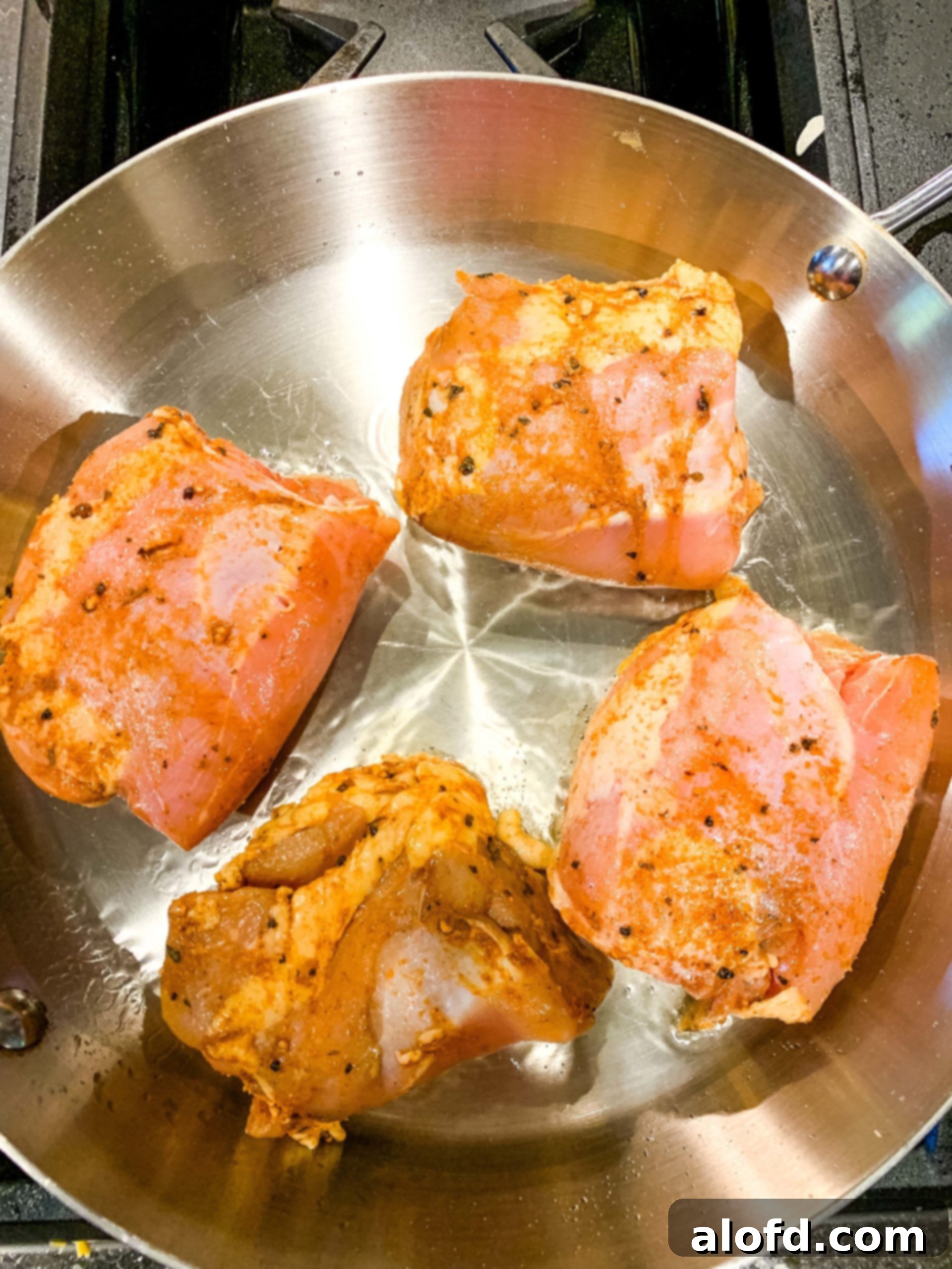 Homestyle Gravy Chicken Thighs 6 Four seasoned chicken thighs sizzling in a hot stainless steel skillet, achieving a perfect golden-brown sear on the stovetop.
