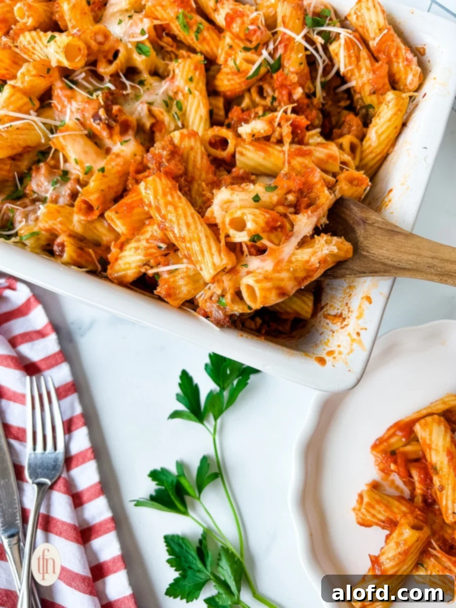 Wooden spoon in a dish of baked rigatoni with sausage, highlighting the rich texture and ingredients.