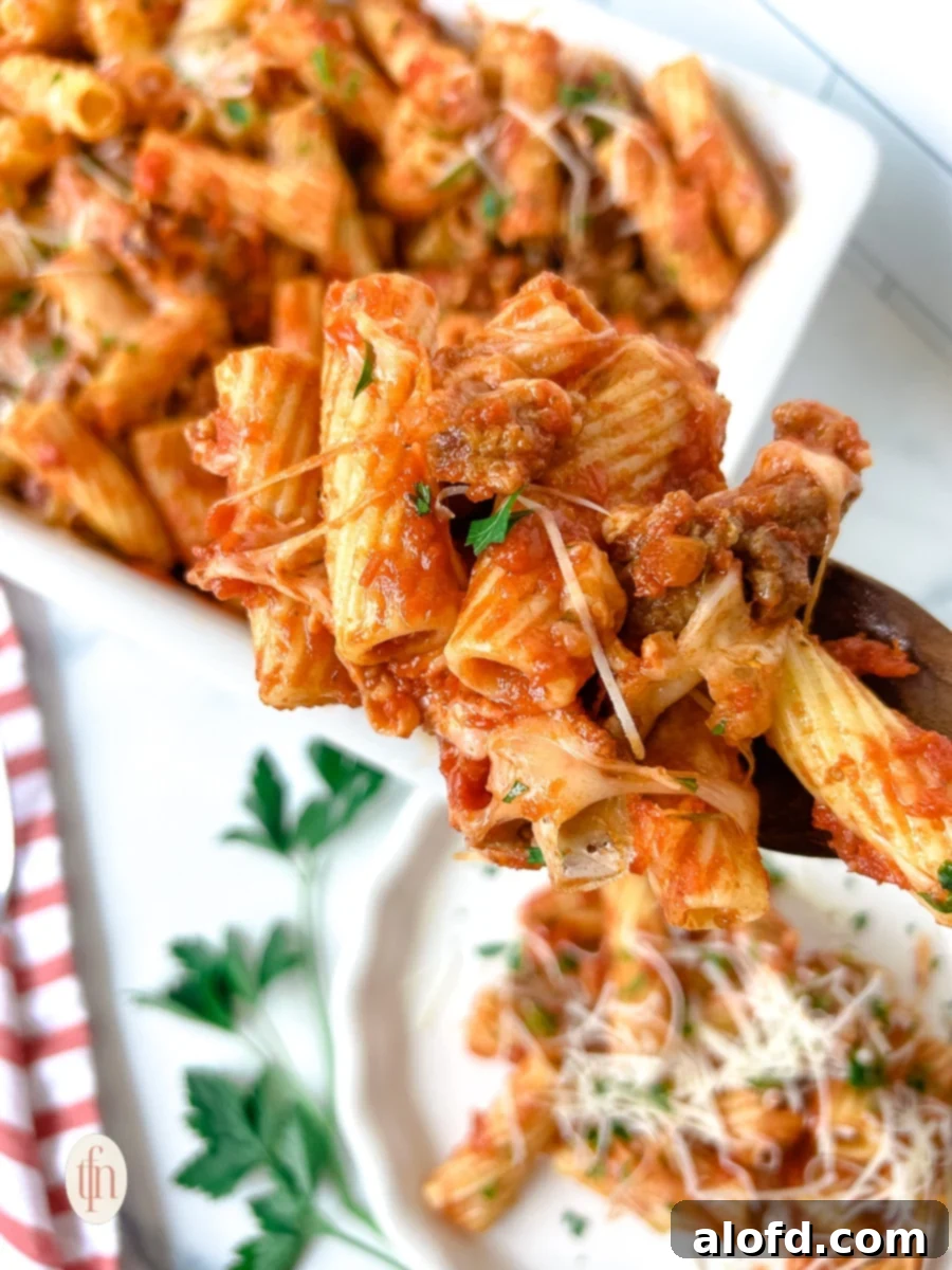 Close-up of a fork lifting sausage rigatoni, showcasing the melted cheese and sauce.
