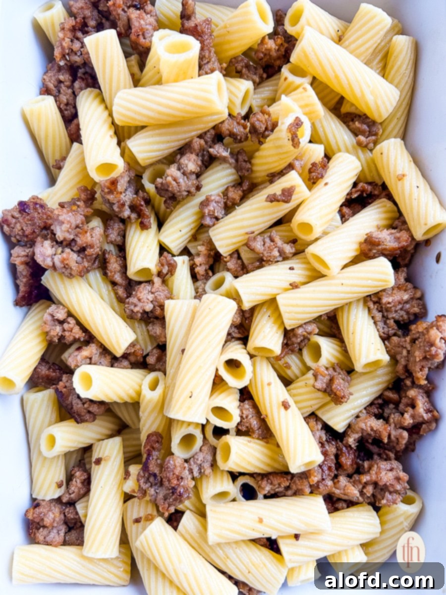 Cooked rigatoni pasta and browned sausage mixed in a casserole dish before adding sauce.