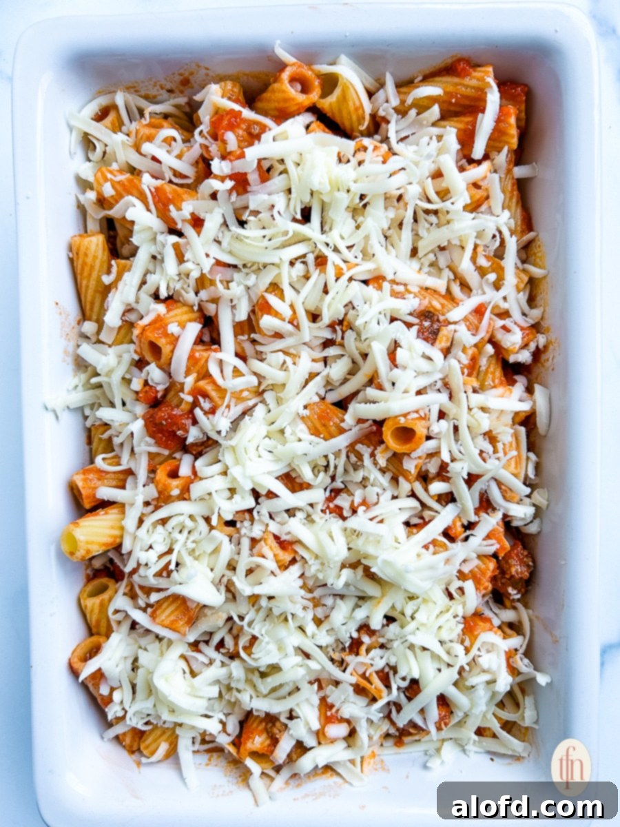 Shredded mozzarella cheese layered over noodles and sauce in a white baking dish, ready for baking.